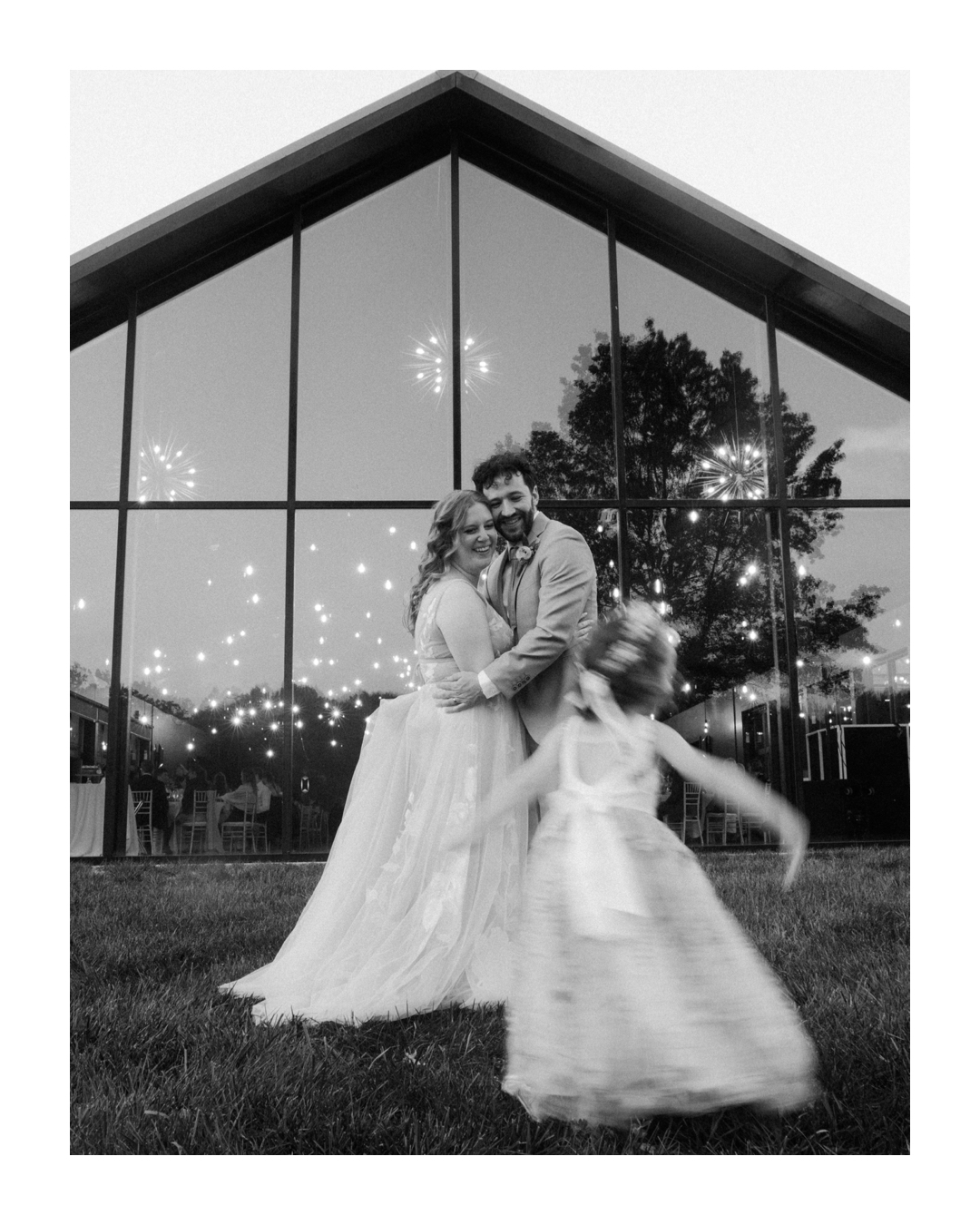 Bride and groom embracing as flower girl twirls in front of them at Jorgensen Farms in Westerville, Ohio, captured by Ashley Wallace Photography. Heartwarming moment with joyful flower girl in a romantic outdoor wedding setting.